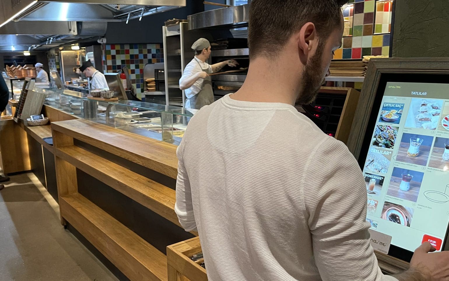 A man is ordering coffee via a terminal; in the background you can see the employees.