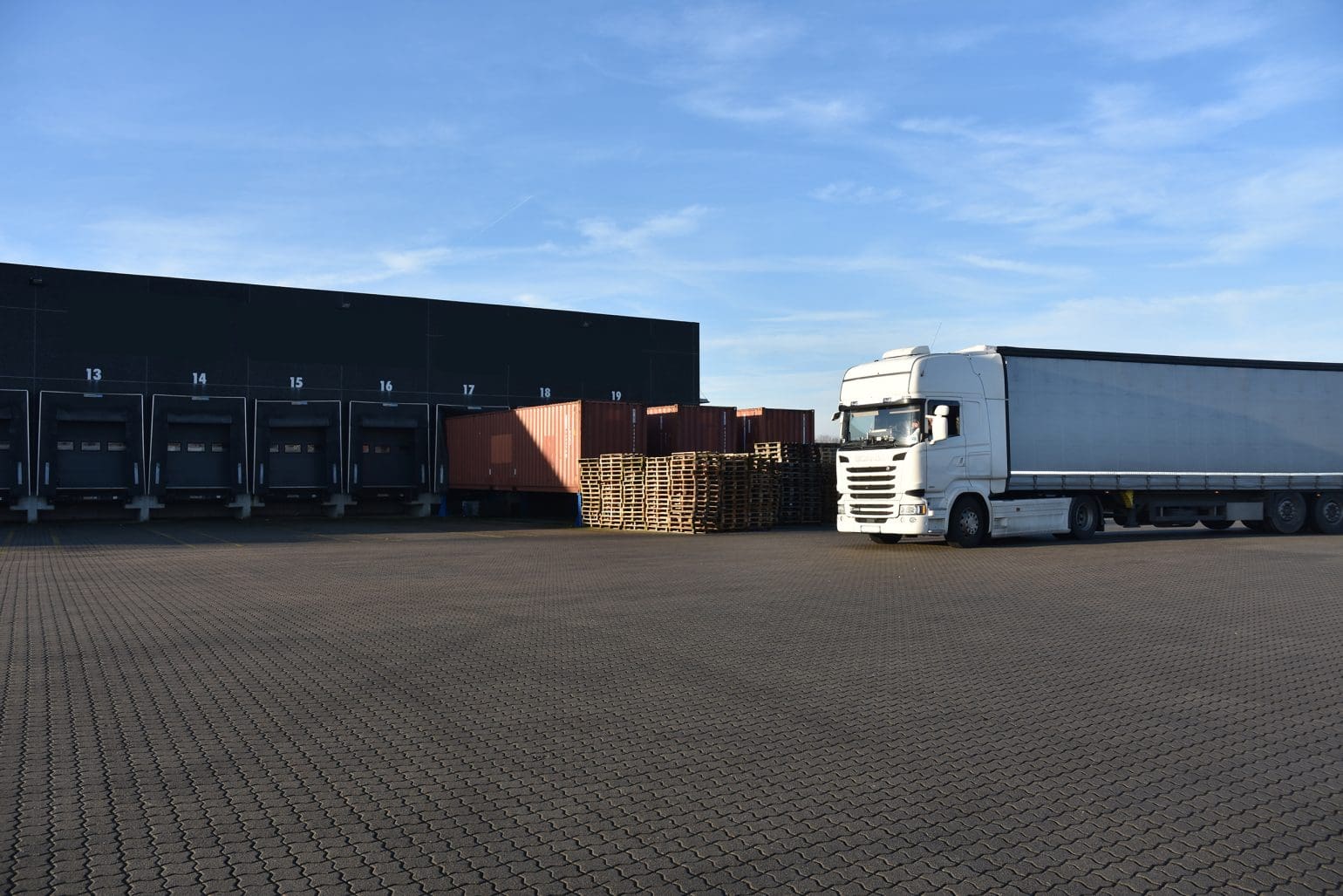 white truck driving past some wooden pallets into a logistics area under blue sky