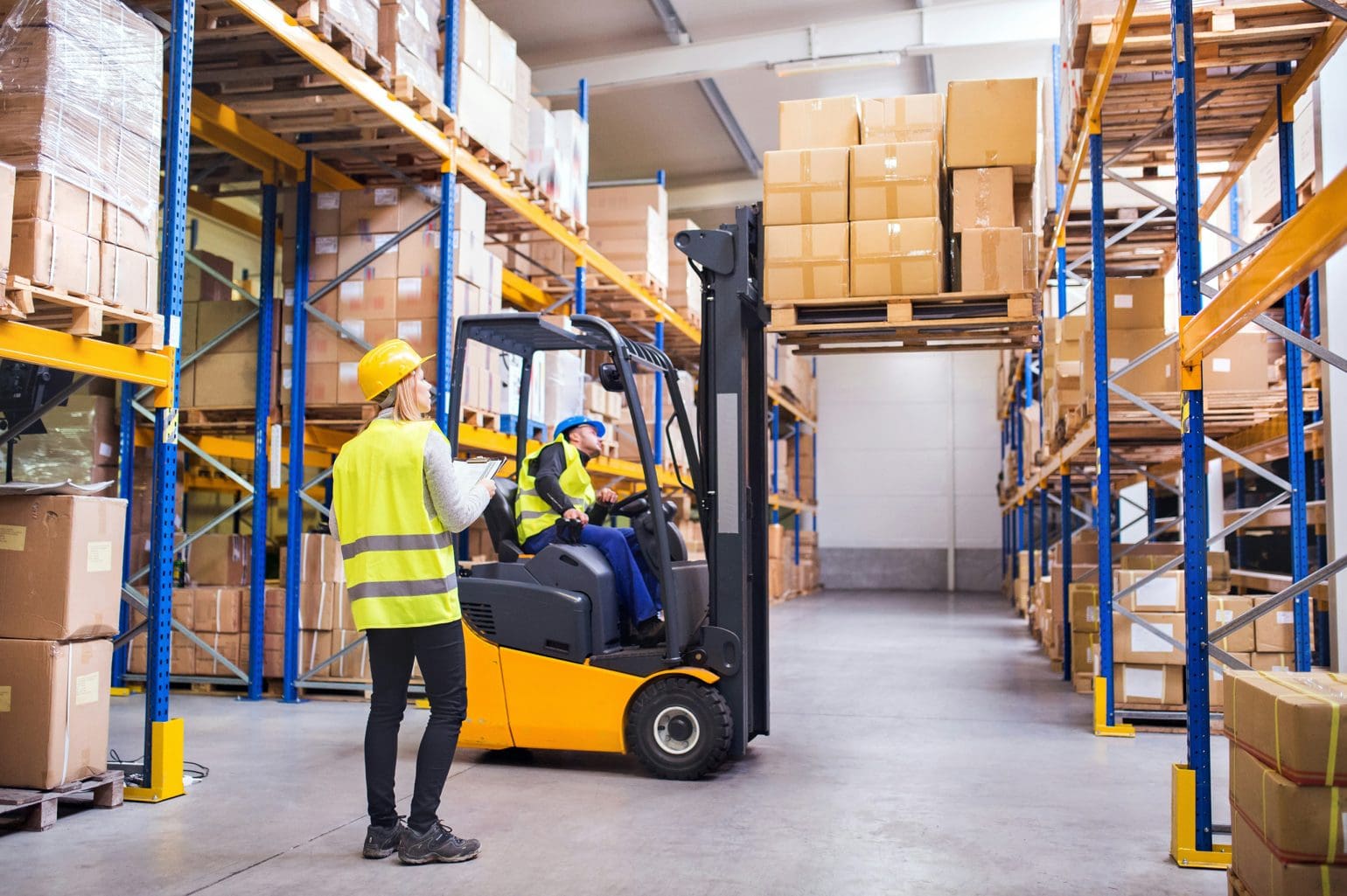 warehouse worker looking at forklift lifting packages into place