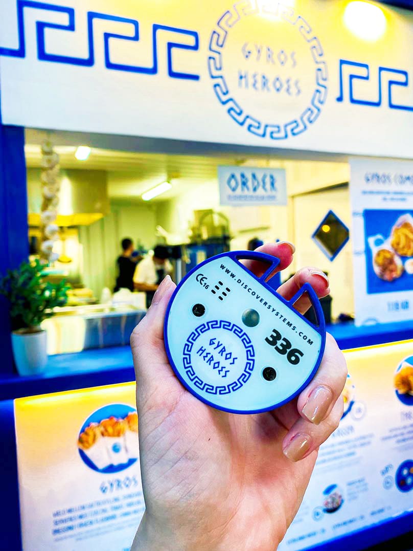 person holding their pager up to the camera with Gyros Heros in the background