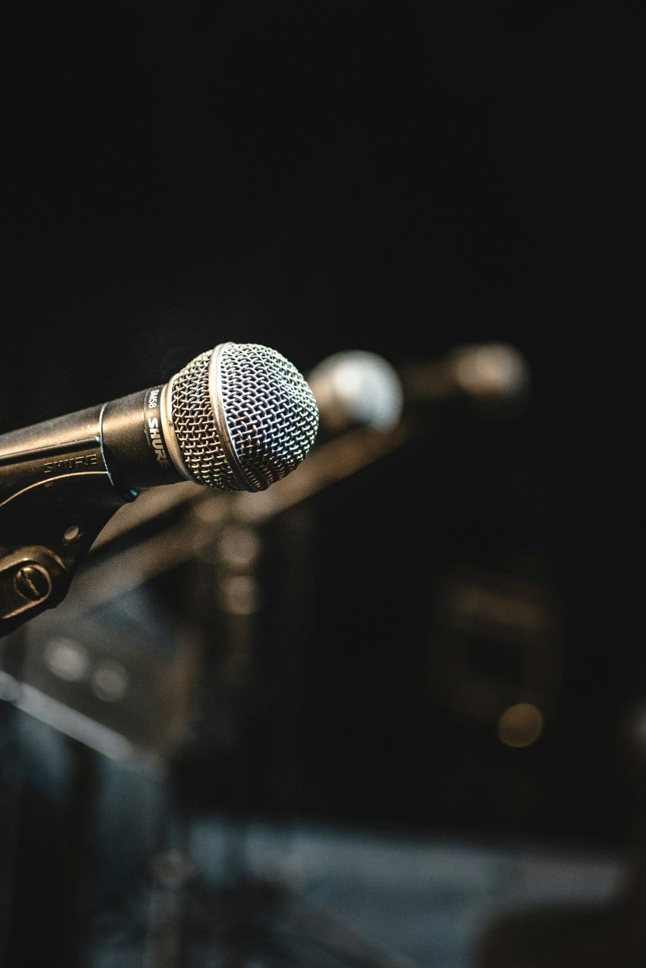 a close-up image of a microphone with 2 other microphones in the background on a stage