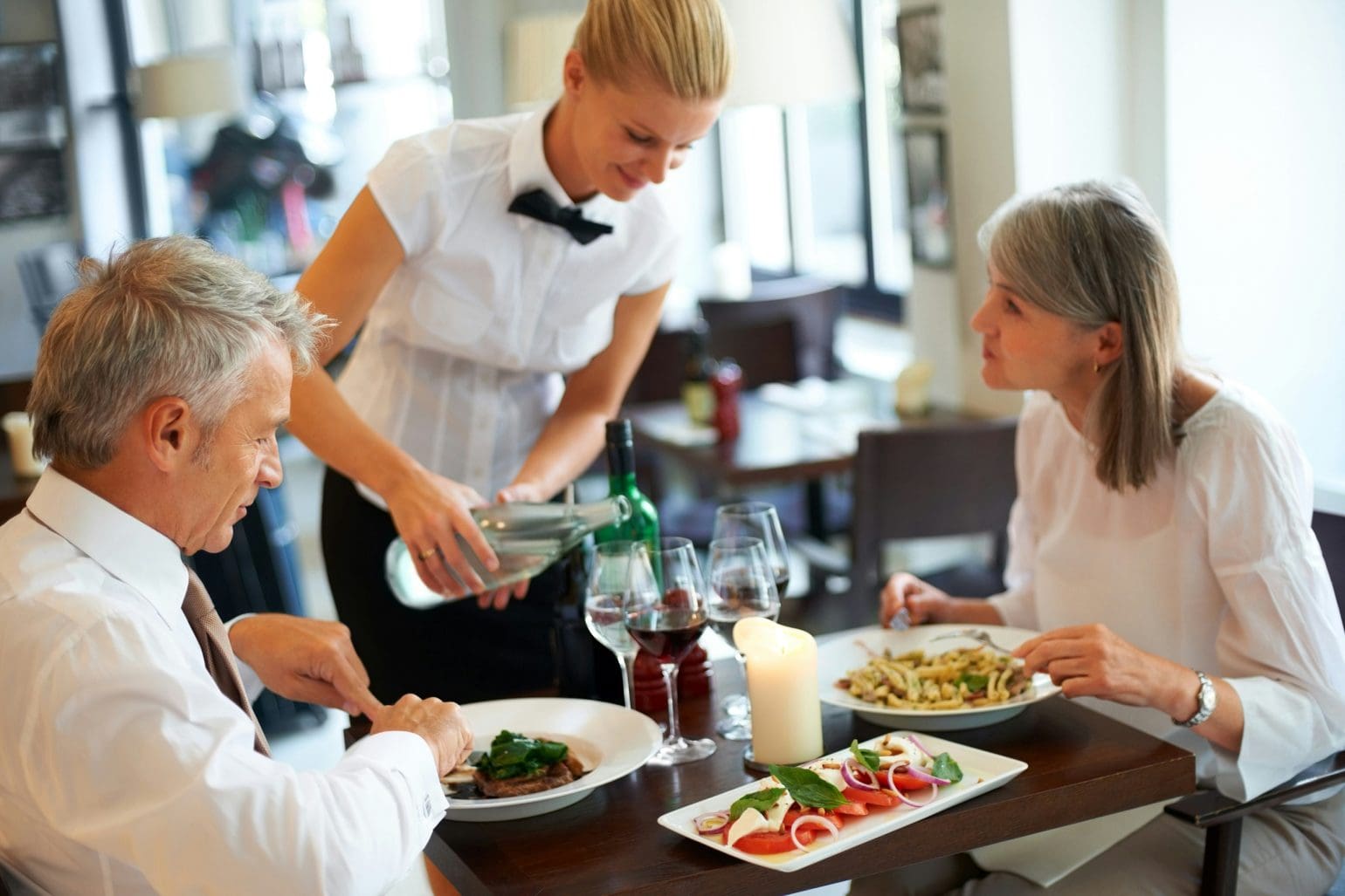 Waiter pours water for customers sitting and having lunch