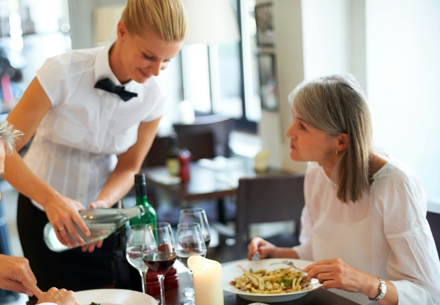 Waiter pours water for customers sitting and eating pasta