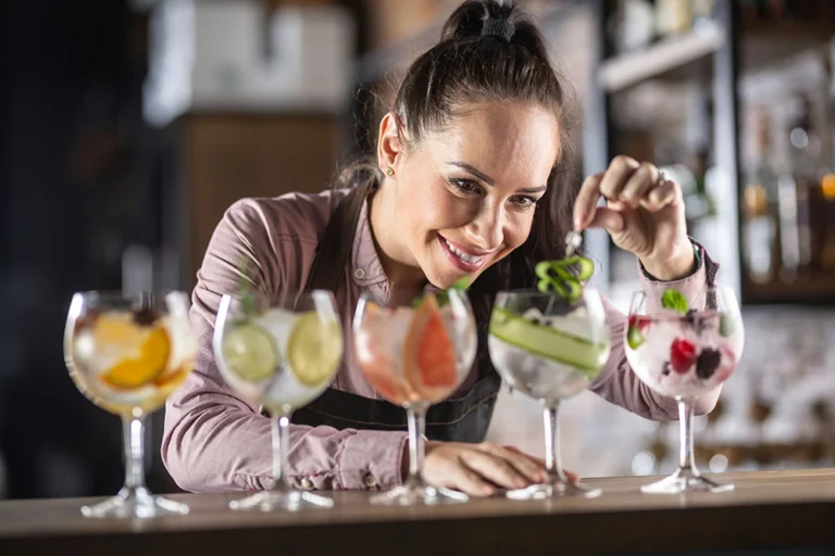 Female server finishing five colorful cocktails in a vibrant restaurant setting – focus on guest service and detail.